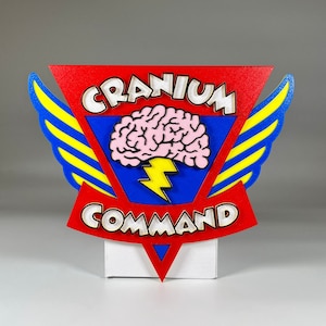 Peut inclure: Une enseigne en bois rouge, bleue et jaune avec un éclair et un graphique de cerveau. L'enseigne indique "Cranium Command".