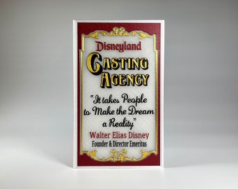 Puede incluir: Un letrero rojo y dorado con el texto "Disneyland Casting Agency" y la cita "Se necesitan personas para hacer que el sueño se haga realidad" de Walter Elias Disney, fundador y director emérito.