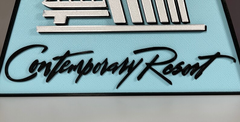 May include: A blue and white sign with the text "Contemporary Resort" in black cursive lettering.