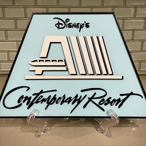 May include: A light blue triangular sign with black trim and white lettering. The sign features a stylised image of the monorail and the text "Disney's Contemporary Resort".