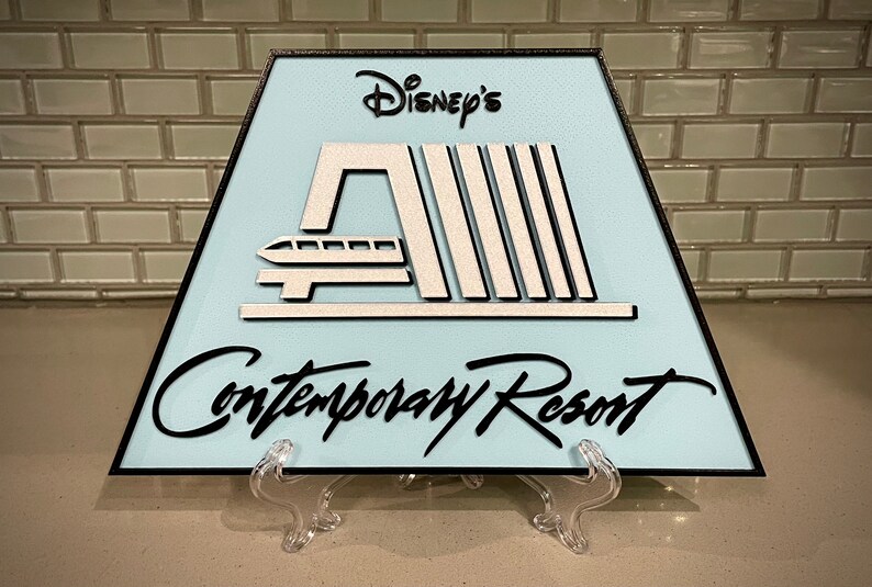 May include: A light blue triangular sign with black trim and white lettering. The sign features a stylised image of the monorail and the text "Disney's Contemporary Resort".