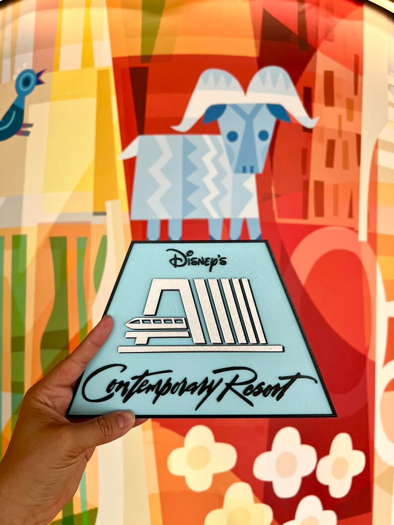 May include: A blue and white triangular sign with black text that reads "Disney's Contemporary Resort". The sign features a stylised image of the monorail and the resort's logo.
