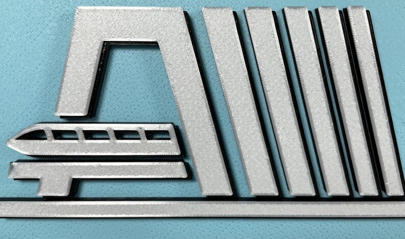 May include: A silver metal logo featuring a stylised train and the words "Walt Disney World" in black lettering.