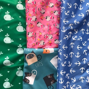 May include: Four different fabric swatches with repeating patterns. The first swatch is green with white whale silhouettes. The second swatch is pink with white Hello Kitty silhouettes. The third swatch is teal with white and black cat silhouettes and the text "CATS". The fourth swatch is blue with white anchor silhouettes.