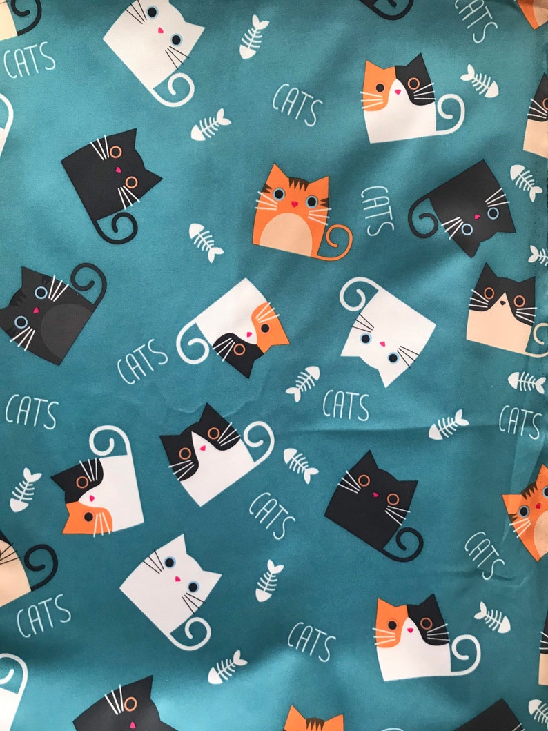 May include: A teal blue fabric with a repeating pattern of black, white, orange, and brown cats. The cats are in various poses and have different facial expressions. The fabric has the word "CATS" printed in white throughout the pattern.