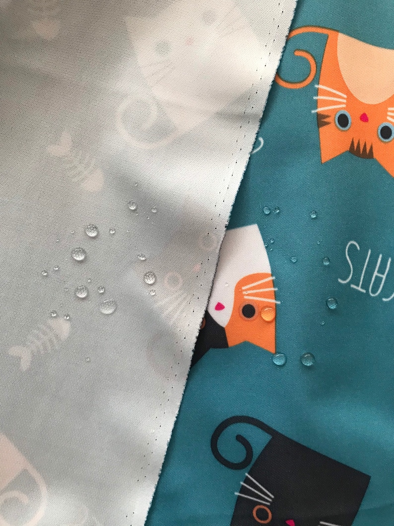May include: A close-up of a teal fabric with a white, orange, and black cat print. The fabric is waterproof and has water droplets on it. The text "Cats" is visible in the background.