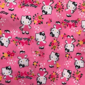 May include: Pink fabric with a repeating pattern of Hello Kitty characters holding flowers. The background is pink with white and yellow flowers. The text "Hello Kitty" appears in the pattern.
