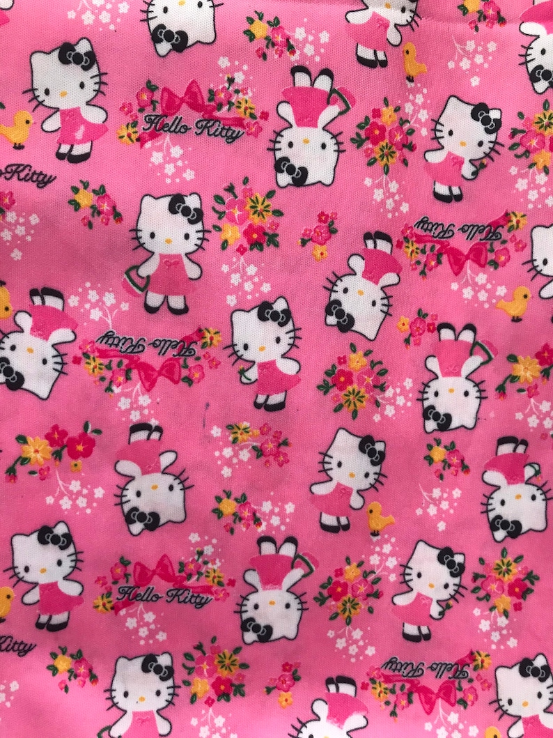 May include: Pink fabric with a repeating pattern of Hello Kitty characters holding flowers. The background is pink with white and yellow flowers. The text "Hello Kitty" appears in the pattern.