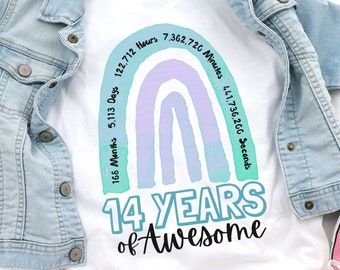 Puede incluir: Camiseta blanca con un diseño de arcoíris y el texto "14 YEARS of Awesome". El arcoíris está hecho de colores pastel y tiene números a su alrededor que representan el tiempo en meses, días, horas, minutos y segundos en 14 años.