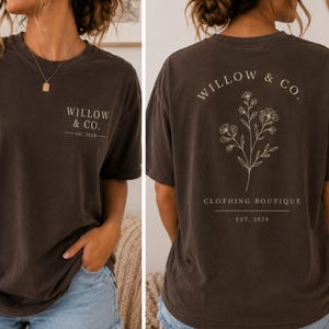 May include: A dark charcoal gray short-sleeve t-shirt featuring the text WILLOW & CO. est. 2024 on the front chest. The back displays a botanical line drawing of wildflowers with the text WILLOW & CO. CLOTHING BOUTIQUE and est. 2024 below.