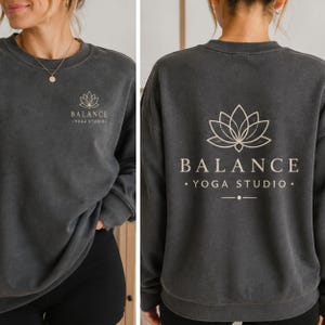 May include: A charcoal gray crewneck sweatshirt featuring a small white lotus flower graphic and the text BALANCE YOGA STUDIO on the left chest, with a larger version of the same lotus graphic and text printed on the back of the garment.