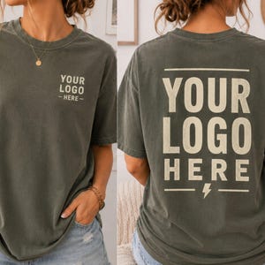 May include: A dark gray short-sleeve t-shirt featuring the text YOUR LOGO HERE printed in a light beige color. The front displays the text on the left chest, while the back features the same text in a larger size with a lightning bolt icon.