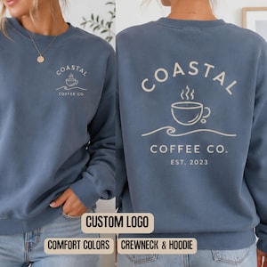 May include: A slate blue crewneck sweatshirt featuring a cream-coloured graphic of a coffee cup and waves with the text Coastal Coffee Co. on the back and a smaller version of the same logo on the front left chest area.