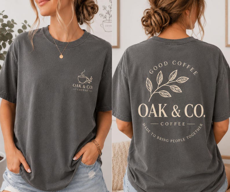 May include: A charcoal gray short-sleeve t-shirt featuring a small coffee cup graphic and the text OAK & CO. COFFEE on the front left chest. The back displays a large leaf illustration with the text GOOD COFFEE OAK & CO. COFFEE MADE TO BRING PEOPLE TOGETHER.