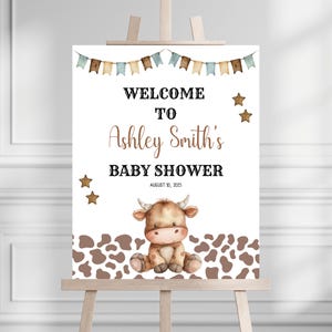 May include: A baby shower welcome sign on an easel. The sign reads "Welcome to Ashley Smith's Baby Shower" with the date August 10, 2025. The design includes a watercolor illustration of a cow, stars, and a banner.