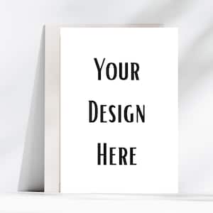 May include: A white greeting card with the words "YOUR DESIGN HERE" in black, leaning against a white background. The card is blank, offering space for a custom design or message.