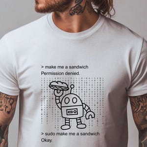 Può includere: T-shirt bianca con grafica in bianco e nero di un robot che tiene un panino. Il testo recita "make me a sandwich Permission denied." e "sudo make me a sandwich Okay."