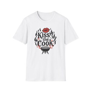 A white t-shirt with a graphic design featuring a pair of lips and flames surrounding the text "Kiss the Cook".