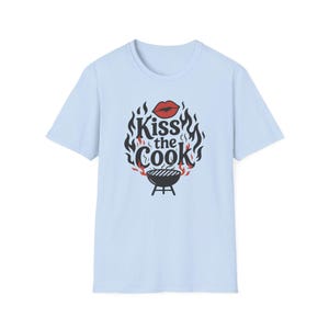 A light blue t-shirt with a graphic design featuring a pair of lips and flames surrounding the text "Kiss the Cook".