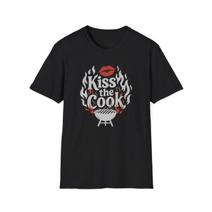 A black t-shirt with a graphic design featuring a pair of lips and flames, along with the text "Kiss the Cook" in a stylized font.