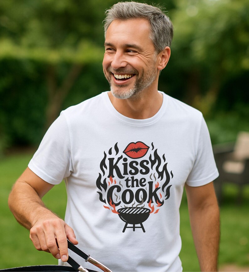 A smiling man wearing a white t-shirt with a graphic design that says "Kiss the Cook".