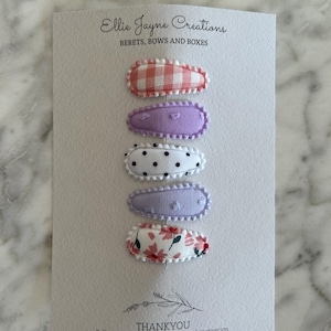 May include: Five fabric-covered hair clips in a variety of patterns. The clips are arranged vertically on a white card with the text "Ellie Jayne Creations" and "BERETS, BOWS AND BOXES" at the top. The bottom of the card reads "THANKYOU Follow us for more on ETSY and instagram".