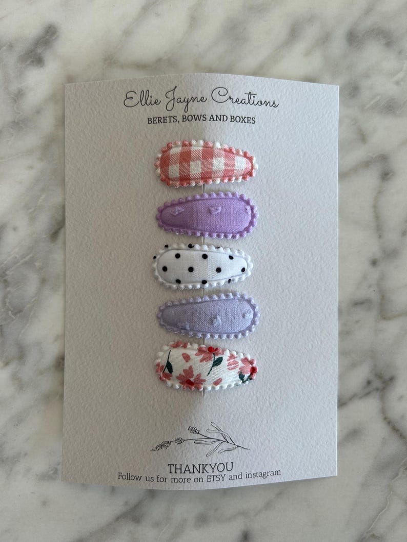 May include: Five fabric-covered hair clips in a variety of patterns. The clips are arranged vertically on a white card with the text "Ellie Jayne Creations" and "BERETS, BOWS AND BOXES" at the top. The bottom of the card reads "THANKYOU Follow us for more on ETSY and instagram".