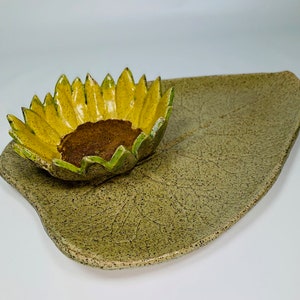 May include: A ceramic serving dish shaped like a green leaf with a yellow and green sunflower-shaped bowl in the center.