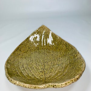 May include: A green ceramic leaf-shaped serving dish with a speckled glaze. The dish is shallow and has a wide, rounded rim.