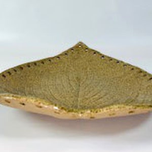 May include: A large, leaf-shaped ceramic serving dish with a textured, green glaze. The dish has a raised, leaf-like design and a scalloped edge.