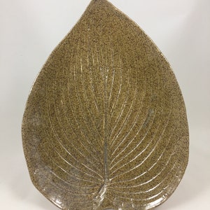 May include: A ceramic leaf-shaped serving dish with a speckled brown glaze. The dish has a raised vein pattern and a slightly rounded edge.