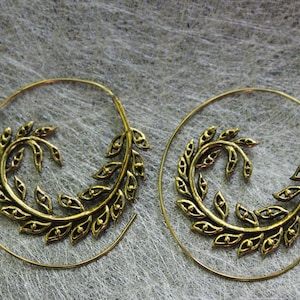 May include: A pair of gold-colored spiral earrings. Each earring features a detailed leaf design that curves around the spiral. The earrings are set against a textured, light gray background.