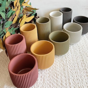 May include: A set of eight ribbed ceramic planters in various colors, including brown, red, yellow, green, and white. The planters are arranged in a row on a white surface.