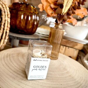 May include: A clear plastic box containing a car diffuser with a white cap and a floral patterned base. The label reads BNL NATURAL DESIGNS, GOLDEN pear orchard, and diffuser base & fragrance oil, long lasting car diffuser 8ml.