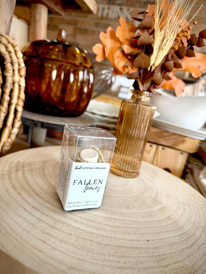 May include: A clear rectangular plastic box containing a small glass bottle with a white cap. The label reads BNL NATURAL DESIGNS and FALLEN LEAVES. The box includes text stating diffuser base, fragrance oil, and long lasting car diffuser 8ml.