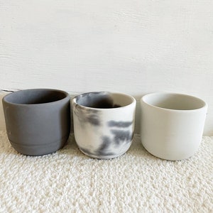 May include: Three small ceramic planters, one gray, one white, and one with a black and white marbled design.