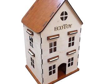 Peut inclure: Un jouet en forme de maison en bois avec un toit marron et des murs de couleur claire. La maison a plusieurs fenêtres, une fenêtre ronde en haut et le texte "ECOTOY" imprimé sur le devant. Le jouet est conçu avec une esthétique simple et épurée.