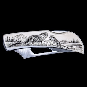 May include: A silver pocket knife with a detailed engraved design of two wolves in a mountain landscape. The knife has a black handle and a silver blade.