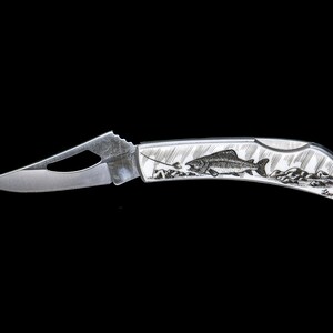 Peut inclure: Un couteau de poche argent&eacute; avec une gravure d&eacute;taill&eacute;e d'un poisson sur le manche. Le couteau a un petit trou dans la lame pour une ouverture facile.