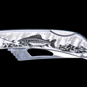 May include: A silver pocket knife with a detailed engraving of a trout jumping out of the water. The knife has a small blade and a handle with the word "Lauder" engraved on it.