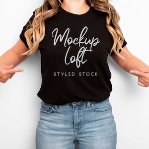 May include: A black t-shirt with the text "Mockup Loft" in white script font. The shirt is being worn by a person with long blonde hair and blue jeans. The text "Styled Stock" is also visible on the shirt.