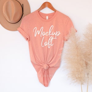 May include: A peach-colored t-shirt with short sleeves and a knotted bottom. The shirt has the text "Mockup Loft" written in white on the front.