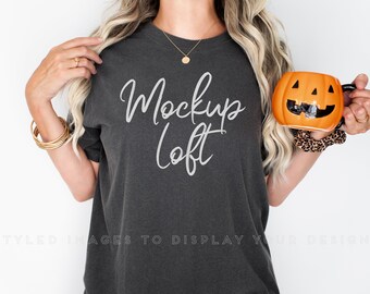 Pode incluir: Uma mulher vestindo uma camiseta cinza escura com o texto "Mockup Loft" em branco. Ela está segurando uma caneca em forma de abóbora com uma alça preta.