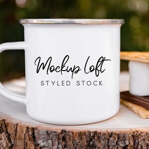 Puede incluir: Taza de esmalte blanco con una inscripción negra que dice "Mockup Loft Styled Stock" sobre una superficie de madera con una galleta graham, chocolate y malvavisco.