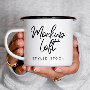 Könnte beinhalten: Eine weiße Emailletasse mit schwarzem Rand und Henkel. Auf der Tasse steht "Mockup Loft" und "Styled Stock".