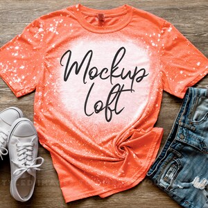 May include: Orange bleached t-shirt with a white bleached circle in the center. The text "Mockup Loft" is written in black inside the circle.