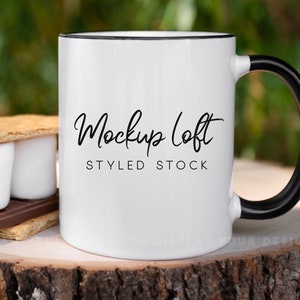 May include: White ceramic mug with a black rim and handle. The mug has the text "Mockup Loft STYLED STOCK" printed on the front.