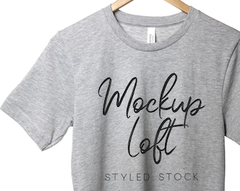 May include: A heather gray t-shirt with the text "Mockups Loft" in black script font and the words "Styled Stock" in black below the script.