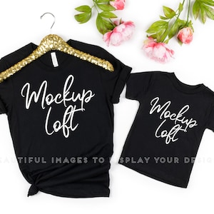 May include: Two black t-shirts with the text "Mockup Loft" in white on a white background. The larger shirt is on a hanger and the smaller shirt is laid flat.