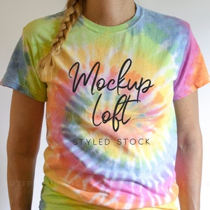 May include: A tie-dye t-shirt with a swirl pattern in shades of pink, yellow, blue, and green. The shirt has the text "Mockup Loft Styled Stock" printed on the front.